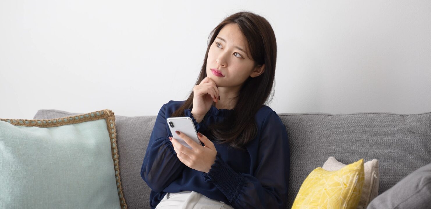スマホを手に持って悩んでいる女性