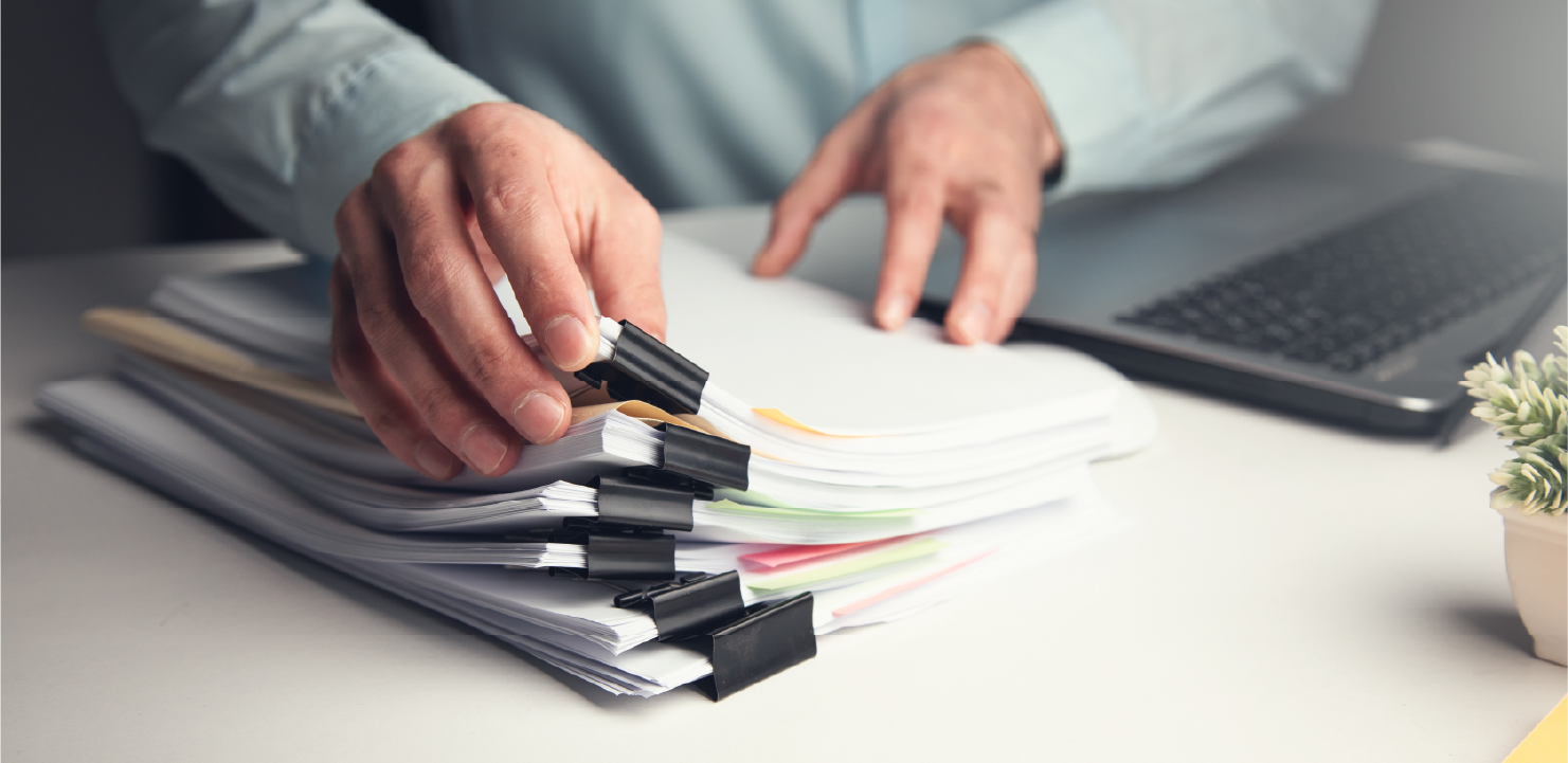 書類の束とノートPCを使用している男性の手元