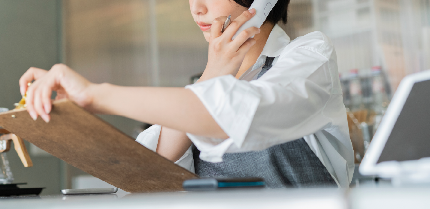 電話を受けながらクリップボードを見る女性店員